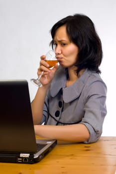 Beautiful asian business woman celebrating her success with wine in front of her computer
