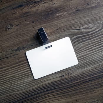 Photo of blank white plastic badge on wood table background. Blank id card. Template for your design. Top view.