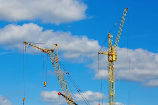 Yellow tower crane and mobile construction crane against blue sky background