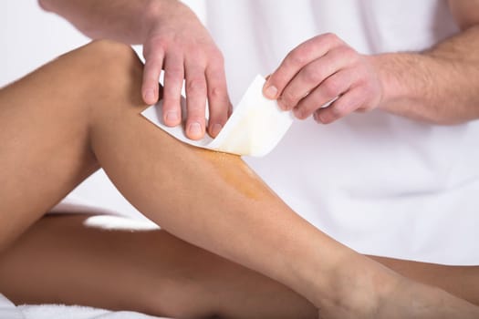 Therapist Waxing Woman's Leg With Wax Strip In Beauty Spa