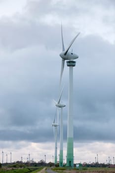 Wind turbine in a row standing in front of cloudy sky at dusk.
