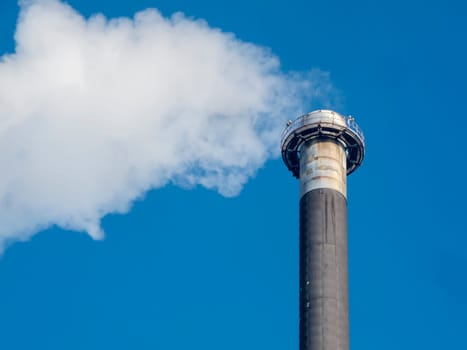 View of an industrial chimney of a power plant with white smoke in front of a blue sky
