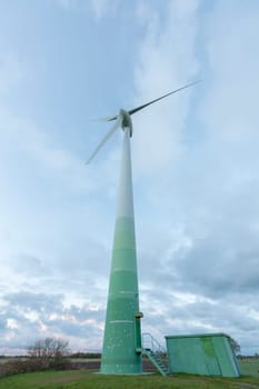 Single wind turbine in the foreground in East Frisia with cloudy skies at dusk.