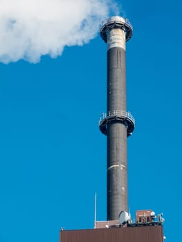 View of an industrial chimney of a power plant with white smoke in front of a blue sky