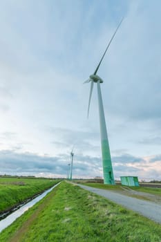 Single wind turbine in the foreground in East Frisia with cloudy skies at dusk.