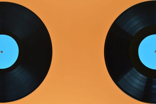 two old black vinyl records with blank cyan labels on orange background