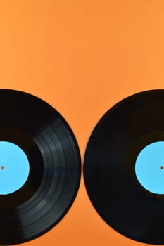 two old black vinyl records with blank cyan labels on orange background