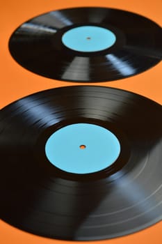 two old black vinyl records with blank cyan labels on orange background