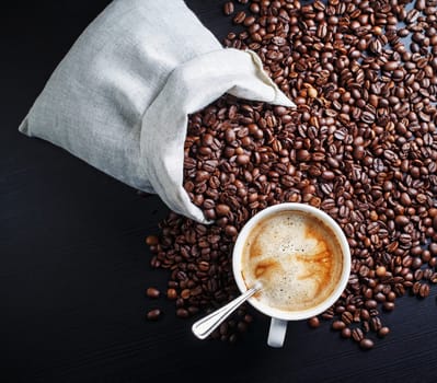 Coffee cup, coffee beans and canvas bag on black table background. Top view.