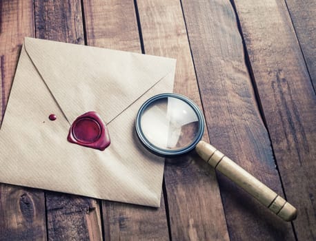 Craft paper envelope and magnifier on wooden background. Responsive design mockup. Vintage stationery. Template for placing your design.