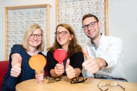 in optician shop-two women and one man with thumb up selecting new glasses