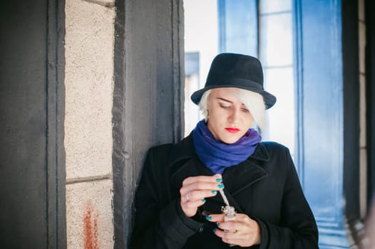 portrait of young beautiful woman with white hair, in a black coat, a skirt and a black hat, smoking an electronic cigarette, blowing the smoke vapor