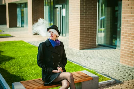 portrait of young beautiful woman with white hair, in a black coat, a skirt and a black hat, smoking an electronic cigarette, blowing the smoke vapor