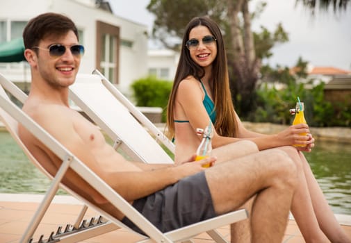 Young couple sitting by the pool and drinking natural juices