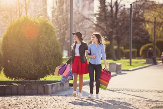 Two girls walking with shopping bags on city streets at sunny day