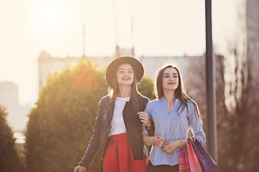 Two girls walking with shopping bags on city streets at sunny day