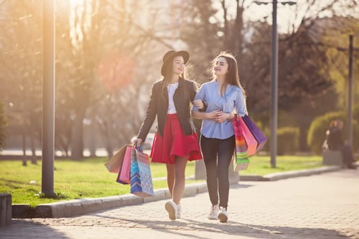 Two girls walking with shopping bags on city streets at sunny day