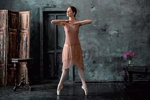 Young and incredibly beautiful ballerina is posing and dancing in a black wooden studio