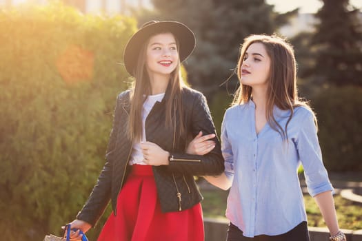 Two girls walking with shopping bags on city streets at sunny day