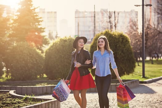 Two girls walking with shopping bags on city streets at sunny day