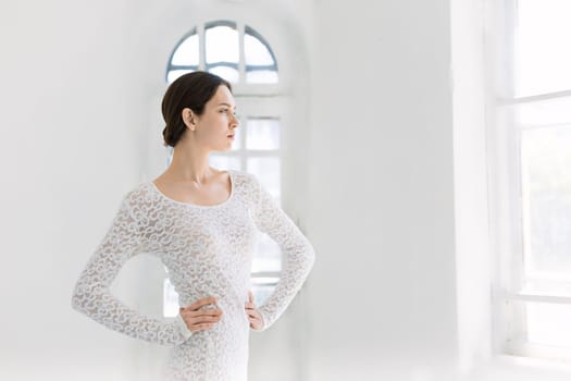 Young and incredibly beautiful ballerina is posing and dancing in a white studio full of light.