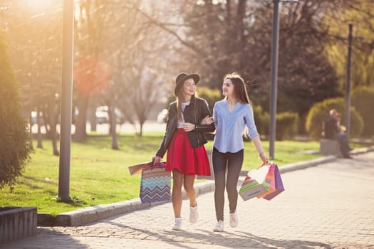 Two girls walking with shopping bags on city streets at sunny day