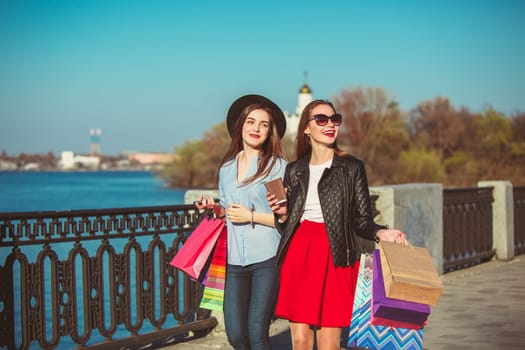 Two girls walking with shopping bags on city streets at sunny day