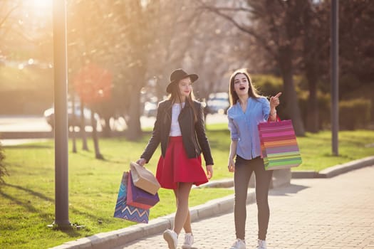 Two girls walking with shopping bags on city streets at sunny day