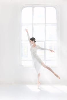 Young and incredibly beautiful ballerina is posing and dancing in a white studio full of light.