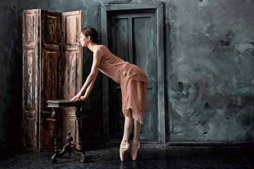 Young and incredibly beautiful ballerina is posing and dancing in a black wooden studio