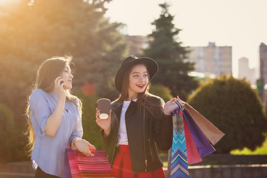 Two girls walking with shopping bags on city streets at sunny day