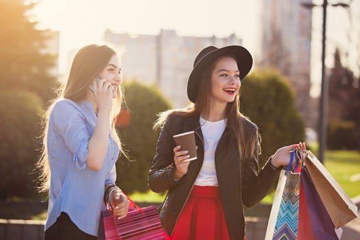 Two girls walking with shopping bags on city streets at sunny day