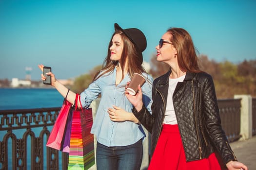 Two girls walking with shopping bags on city streets at sunny day