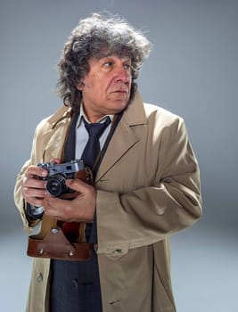 The senior man in cloak as detective or mafia boss with photo camera. Studio shot on gray in retro stile