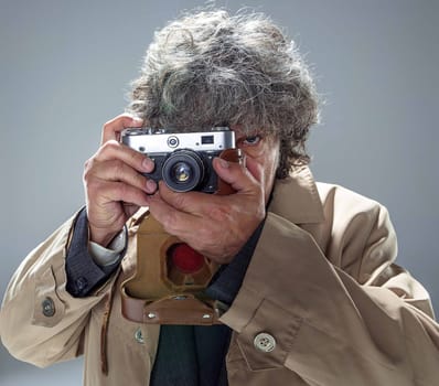 The senior man in cloak as detective or mafia boss with photo camera. Studio shot on gray in retro stile