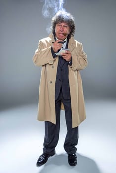 The senior man in cloak as detective or mafia boss writing in a notebook with pen. Studio shot on gray in retro stile
