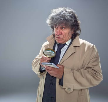 The senior man in cloak as detective or mafia boss with With a magnifying glass. Studio shot on gray in retro stile. Concept of Search