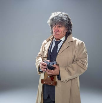 The senior man in cloak as detective or mafia boss with photo camera. Studio shot on gray in retro stile