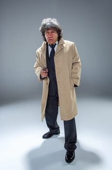 Senior police agent with a gun standing as detective or mafia boss. Studio shot on gray in retro stile