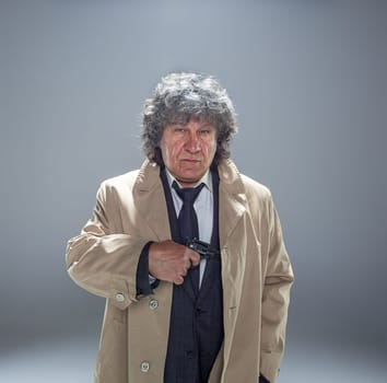 Senior police agent with a gun standing as detective or mafia boss. Studio shot on gray in retro stile
