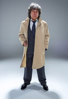 Senior police agent with a gun standing as detective or mafia boss. Studio shot on gray in retro stile