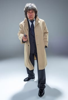 Senior police agent with a gun standing as detective or mafia boss. Studio shot on gray in retro stile