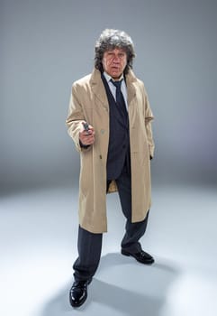 Senior police agent with a gun standing as detective or mafia boss. Studio shot on gray in retro stile