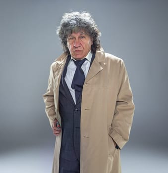 Senior police agent with a gun standing as detective or mafia boss. Studio shot on gray in retro stile