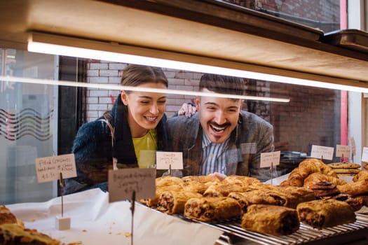 Happy couple are looking into the window of a french bakery. They are laughing as they look at croissants and pastries.