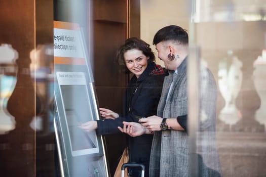 Couple are buying tickets for their train using an electronic ticket machine in the station.