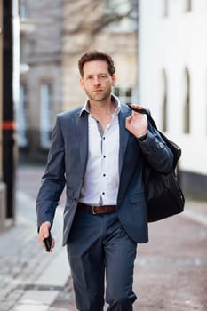Businessman is walking to work through the city. He is carrying a holdall bag and his smart phone.