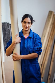 Portrait of a female carpenter at work. She is holding a cardboard tube and is smiling for the camera.