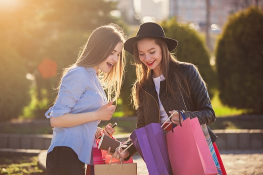 Two girls walking with shopping bags on city streets at sunny day