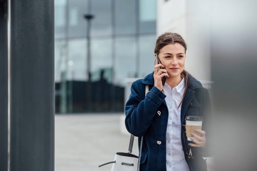 Businesswoman is walking to work in the city. She is holding a coffee cup and is talking on the phone.